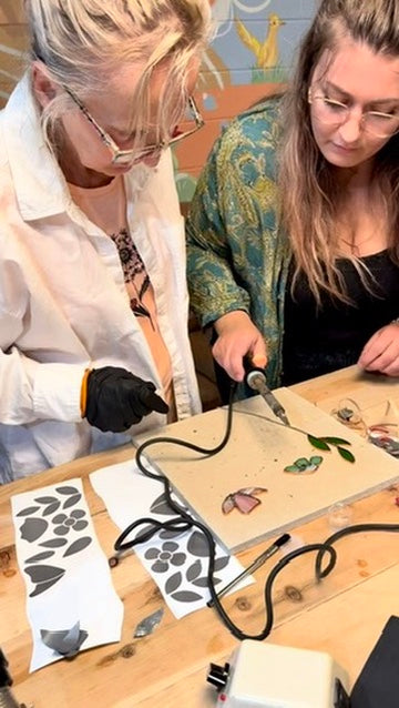 Two people working on a craft project with stencils and tools on a table.