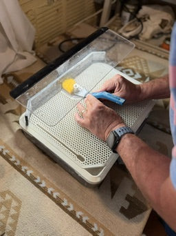 Person using a tool on a small grid board with a patterned rug in the background