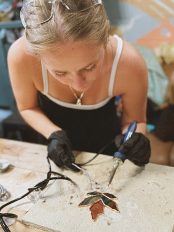 Person using a soldering iron on a piece of jewelry in a workshop setting