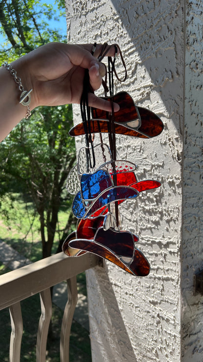 Colorful glass cowboy hats hanging on a string against a neutral wall.